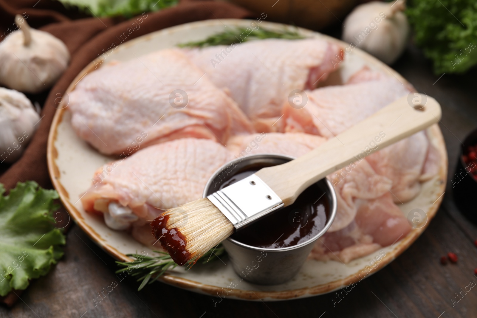 Photo of Plate with fresh marinade, raw chicken and basting brush on wooden table, closeup