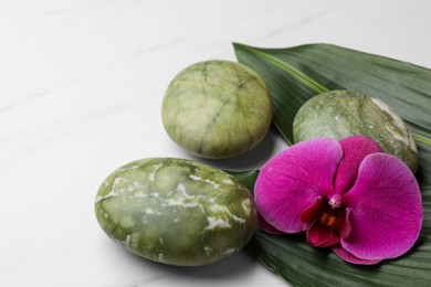 Beautiful spa composition with stones, flower and leaves on white marble table, closeup