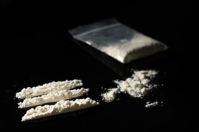 Photo of Drug addiction. Plastic bag with cocaine on black table, closeup