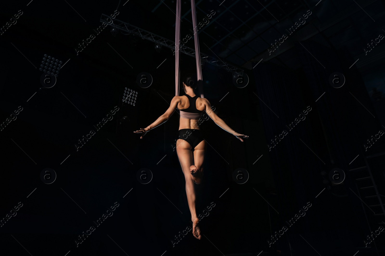 Photo of Young woman performing acrobatic element on aerial silk indoors