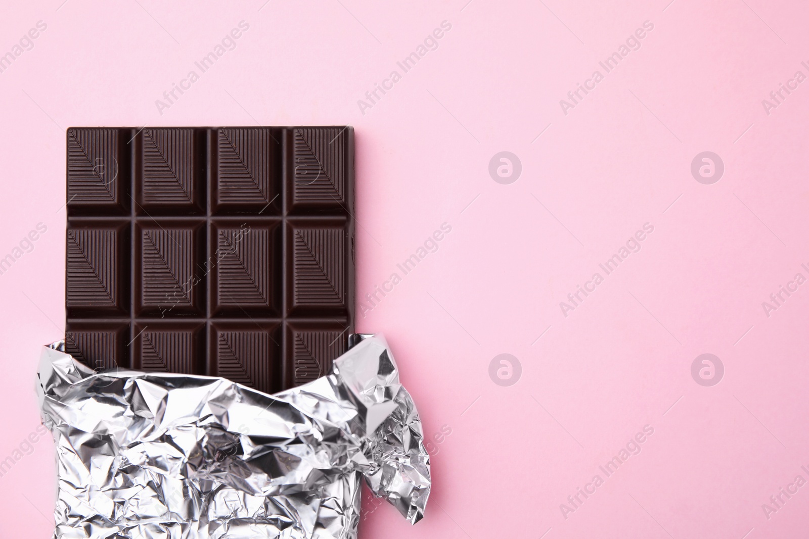 Photo of Tasty chocolate bar on pink background, top view. Space for text