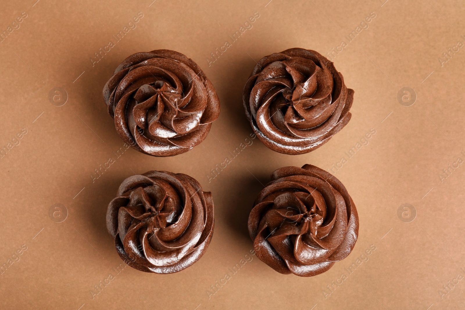 Photo of Delicious chocolate cupcakes with cream on brown background, flat lay