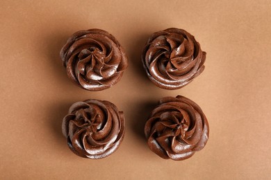 Delicious chocolate cupcakes with cream on brown background, flat lay