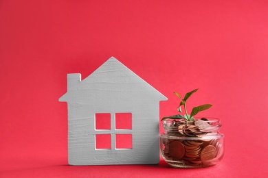 Photo of House model, jar with coins and plant on color background. Space for text