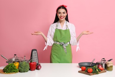 Photo of Young housewife at white table with utensils and products on pink background