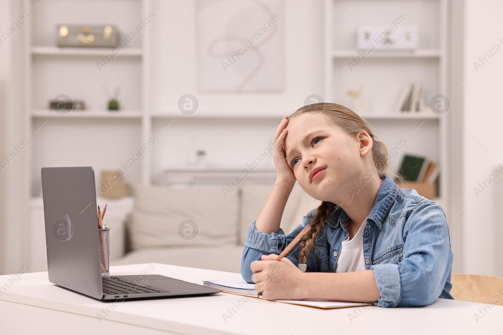 Photo of Little girl suffering from headache while doing homework at home