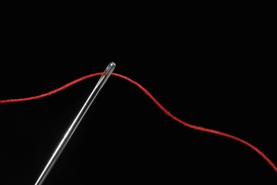 Sewing needle with red thread on black background, closeup