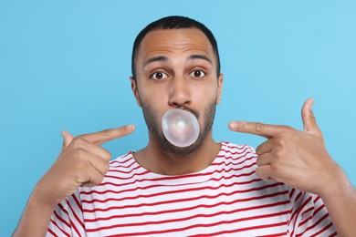 Photo of Portrait of young man blowing bubble gum on light blue background