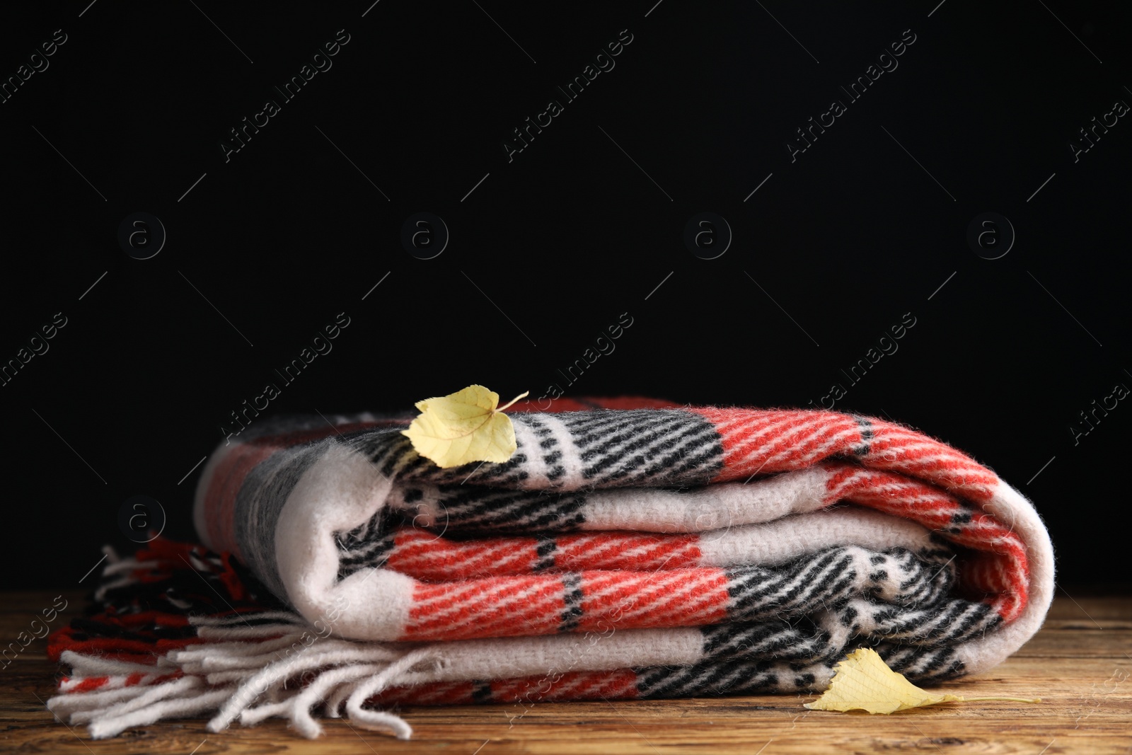 Photo of Checkered plaid and dry leaves on wooden table