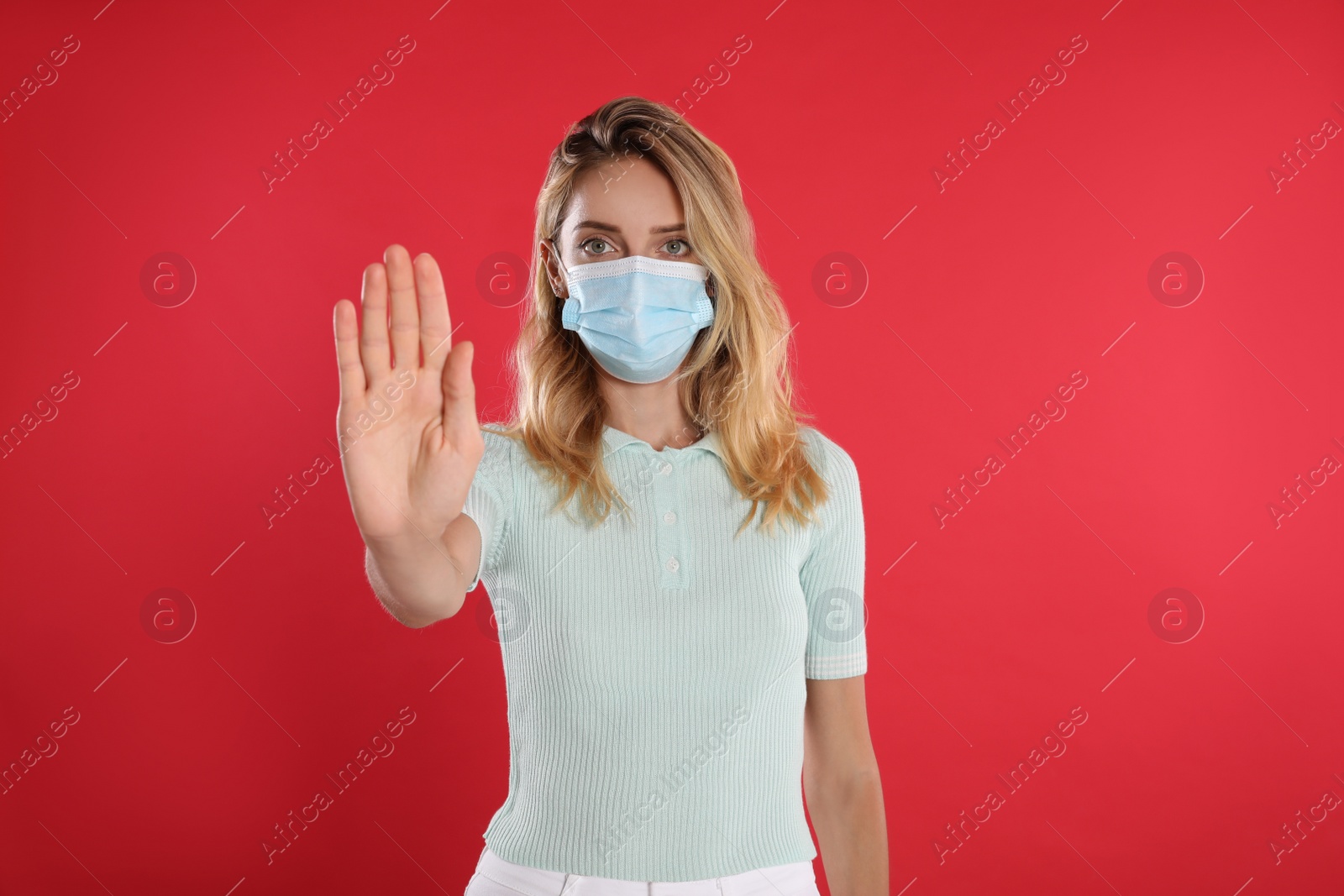 Photo of Woman in protective face mask showing stop gesture on red background. Prevent spreading of coronavirus