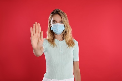 Photo of Woman in protective face mask showing stop gesture on red background. Prevent spreading of coronavirus