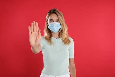 Woman in protective face mask showing stop gesture on red background. Prevent spreading of coronavirus