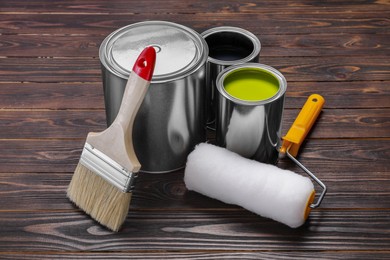 Photo of Cans of yellow and black paints, roller with brush on wooden table