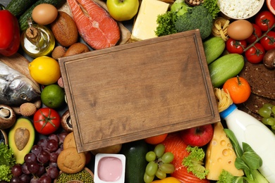Photo of Wooden board among different products, top view with space for text. Healthy food and balanced diet