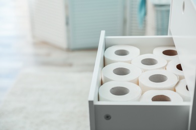 Open cabinet drawer with toilet paper rolls in bathroom. Space for text