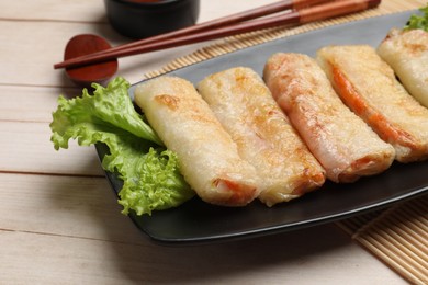 Photo of Delicious fried spring rolls and chopsticks on light wooden table, closeup