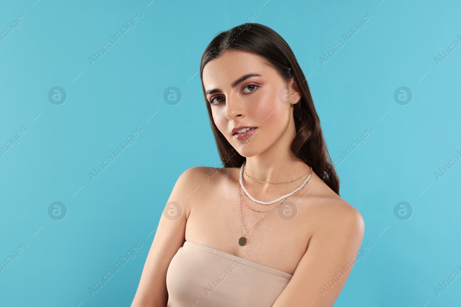 Photo of Beautiful woman with elegant necklaces on light blue background