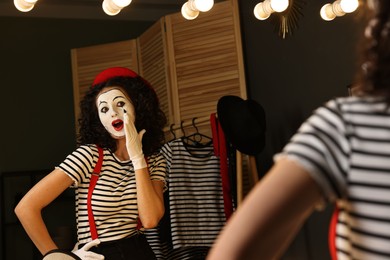Young woman in mime costume posing near mirror indoors