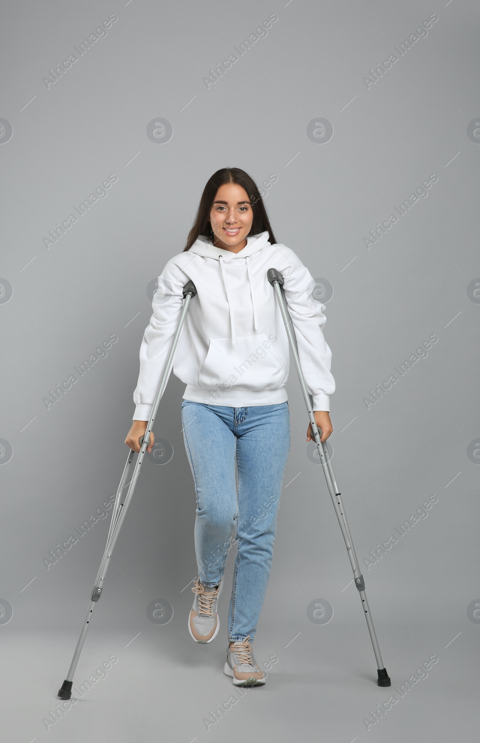 Photo of Young woman with axillary crutches on grey background
