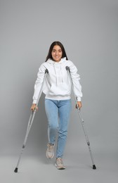 Young woman with axillary crutches on grey background