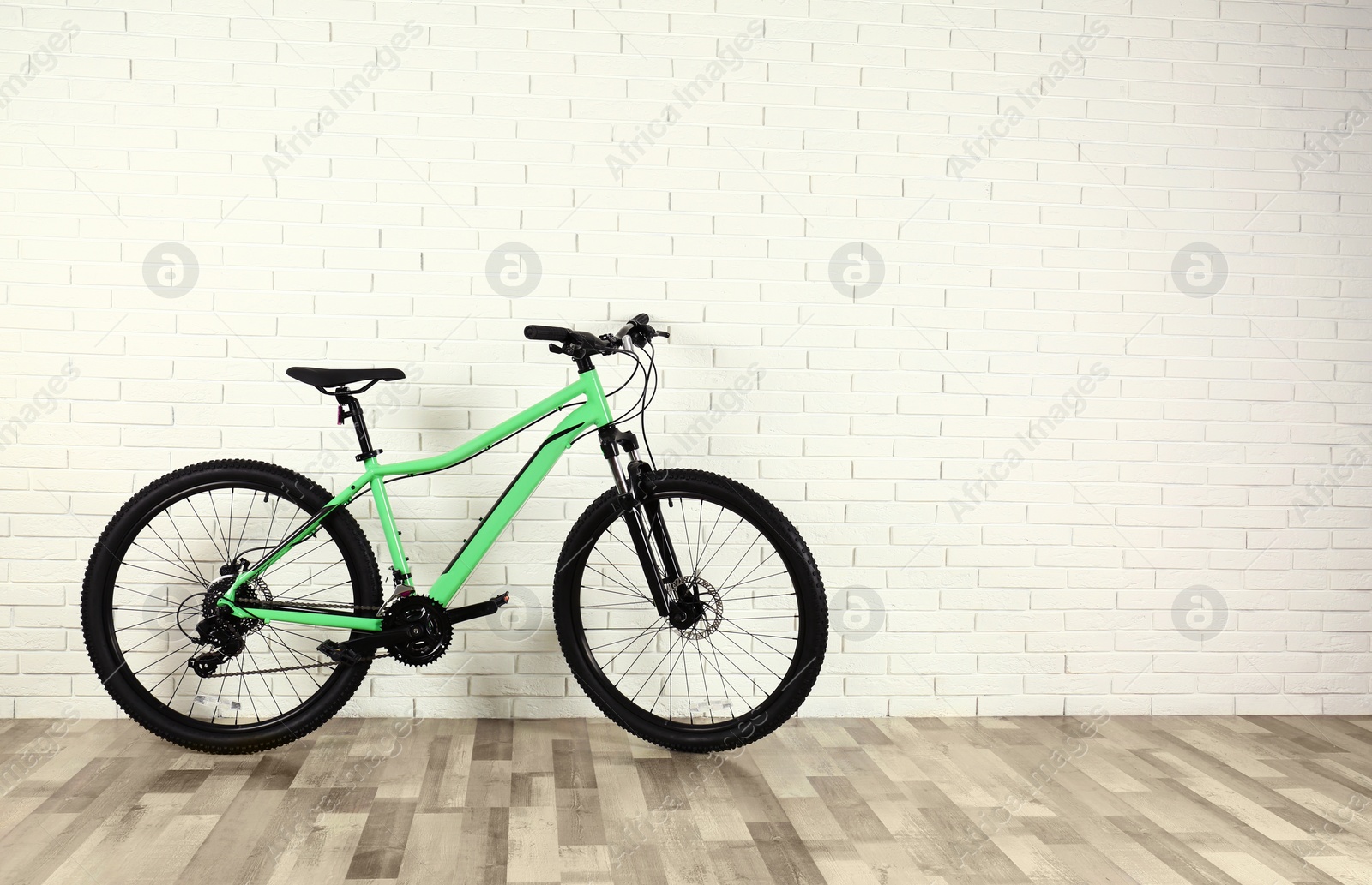 Photo of Modern bicycle near white brick wall indoors. Space for text