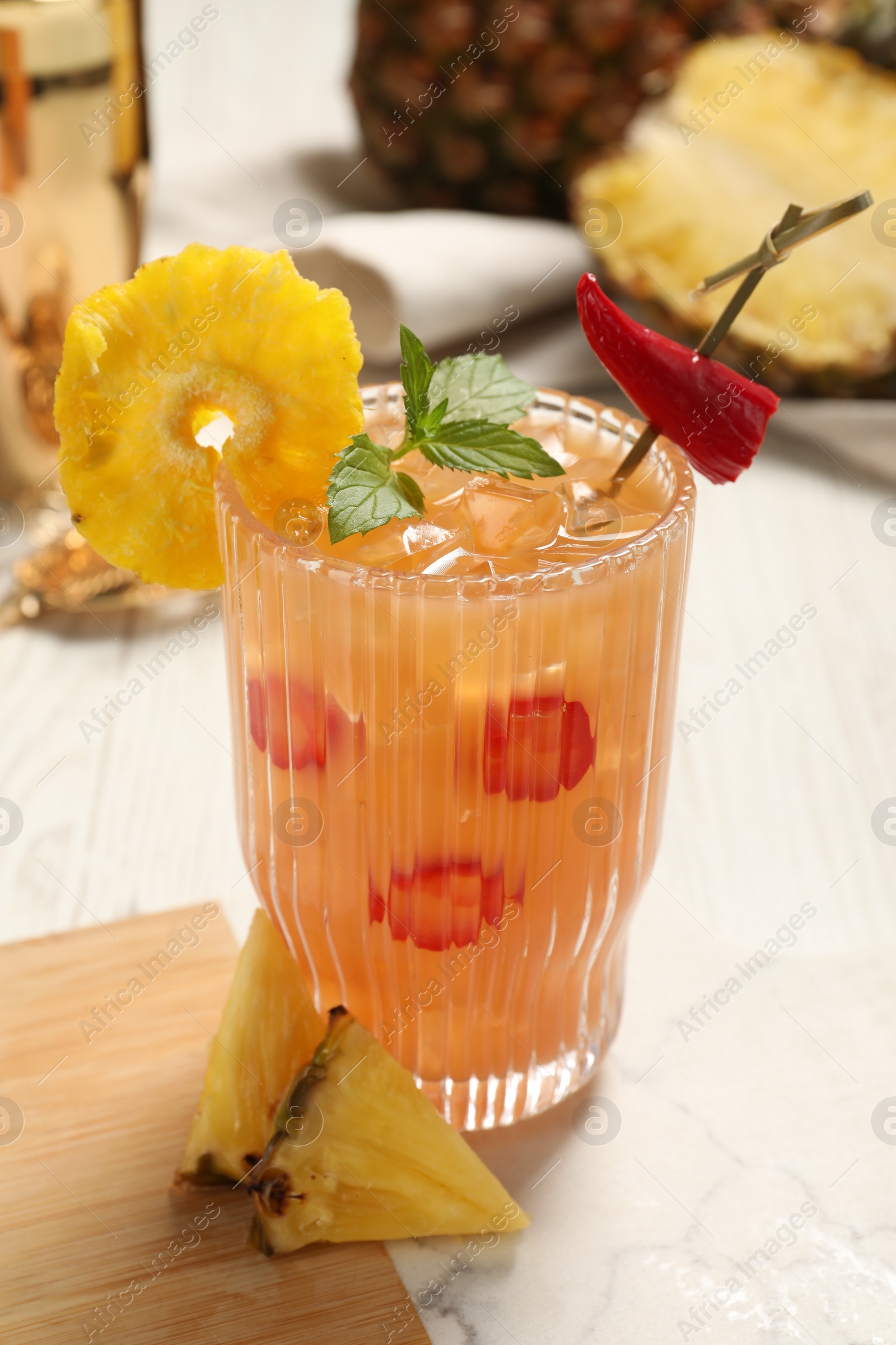 Photo of Glass of spicy pineapple cocktail with chili pepper and mint on white table