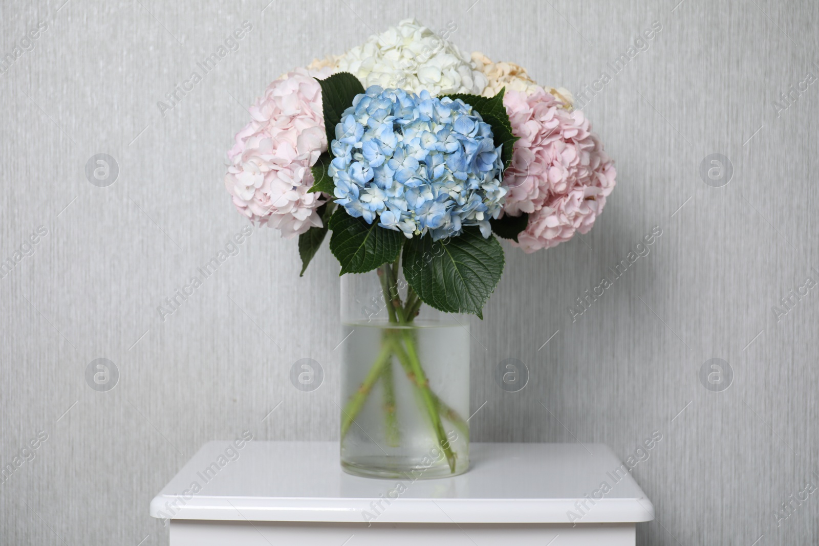 Photo of Beautiful hydrangea flowers in vase on white bedside table near light gray wall
