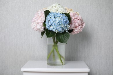 Photo of Beautiful hydrangea flowers in vase on white bedside table near light gray wall