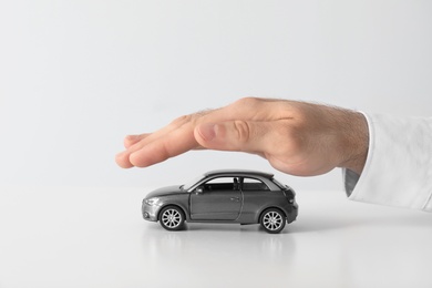 Male insurance agent covering toy car on white background, closeup