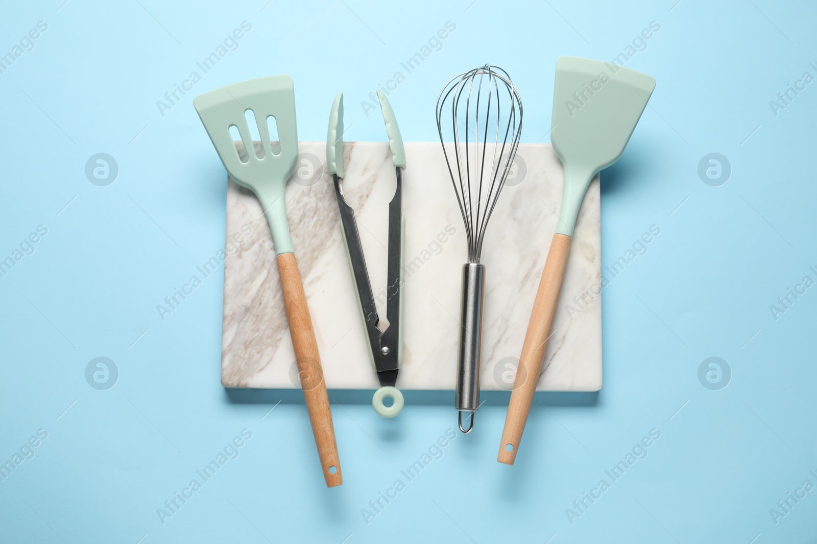 Photo of Different spatulas, whisk and tongs on light blue background, flat lay