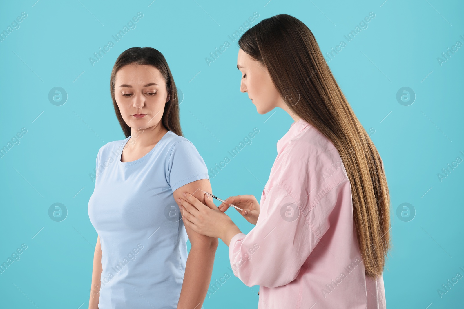 Photo of Woman giving insulin injection to her diabetic friend on light blue background