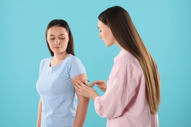 Woman giving insulin injection to her diabetic friend on light blue background