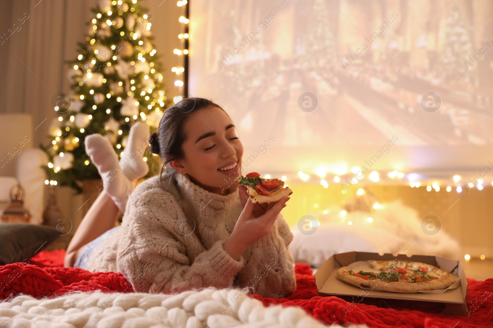 Photo of MYKOLAIV, UKRAINE - DECEMBER 24, 2020: Woman watching Harry Potter and Philosopher's Stone movie via video projector in room. Cozy winter holidays atmosphere