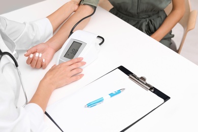 Doctor checking patient's blood pressure at table in office