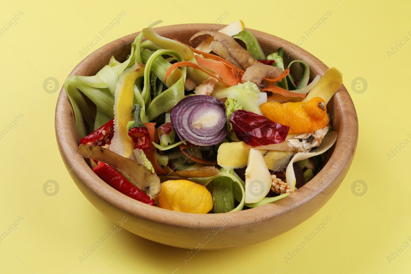 Photo of Peels of fresh vegetables in bowl on yellow background