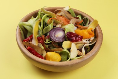 Photo of Peels of fresh vegetables in bowl on yellow background