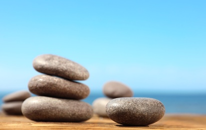 Photo of Stones on wooden table against seascape, space for text. Zen concept