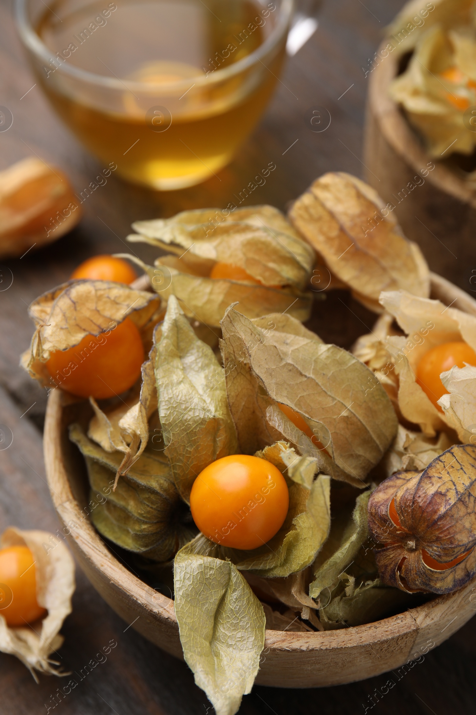 Photo of Ripe physalis fruits with calyxes in bowl on wooden table, closeup