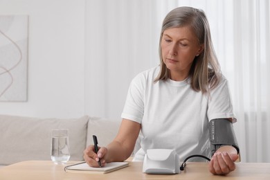 Photo of Woman measuring blood pressure and writing it down into notebook at wooden table in room, space for text