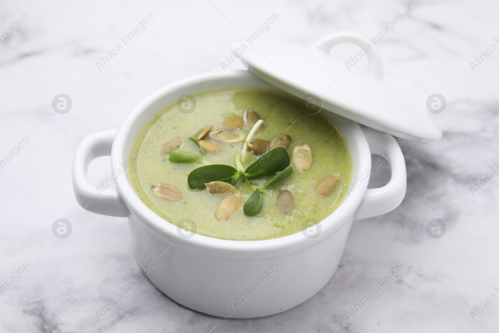 Photo of Delicious broccoli cream soup with pumpkin seeds on white marble table, closeup