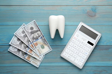 Photo of Ceramic model of tooth, dollar banknotes and calculator on light blue wooden table, flat lay. Expensive treatment