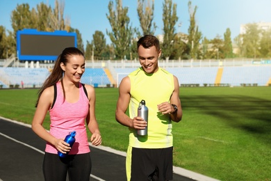 Young sporty couple holding bottles of water at stadium on sunny day
