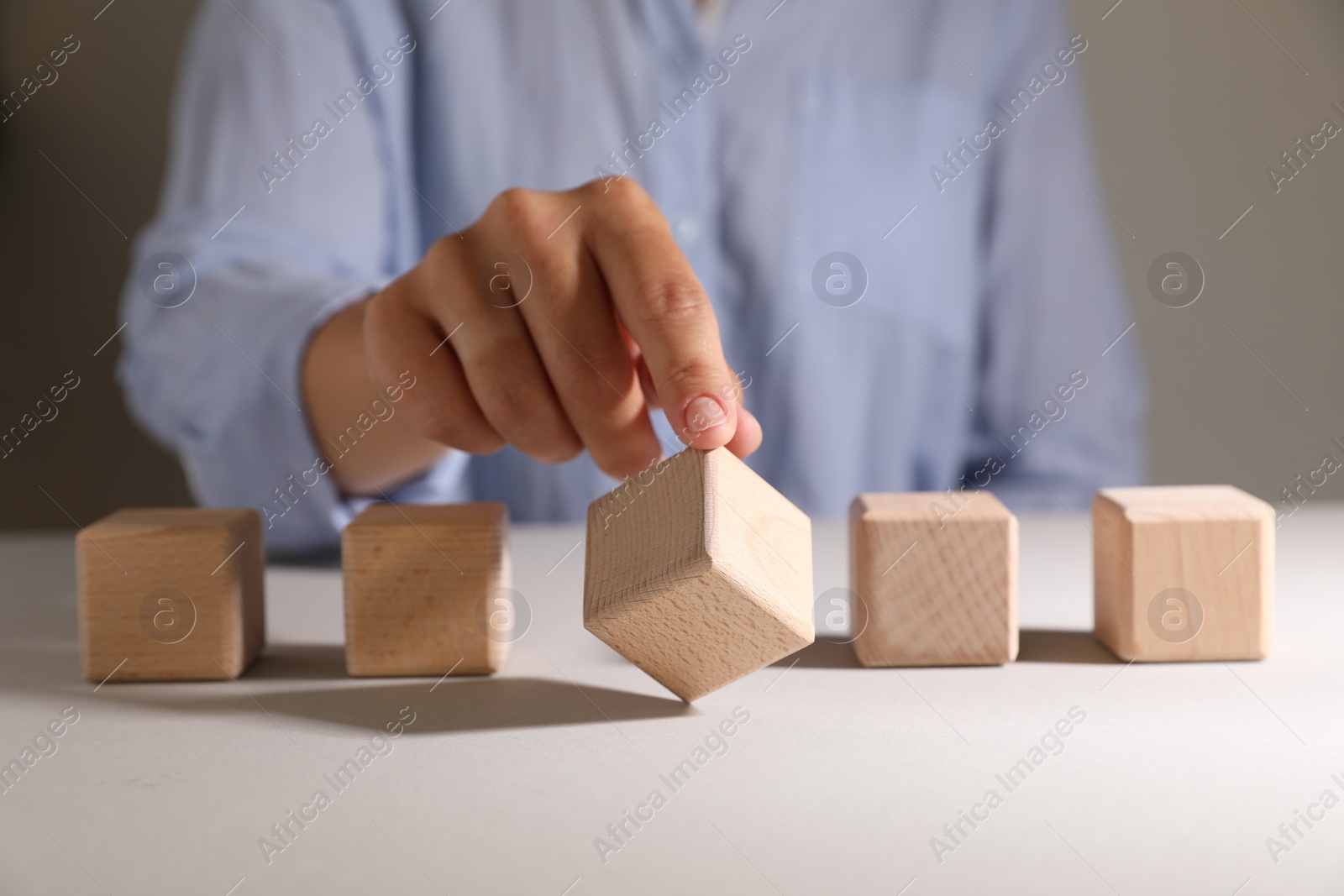 Photo of Woman choosing wooden cube among others at white table, closeup