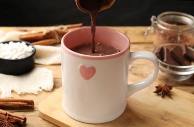 Photo of Pouring tasty hot chocolate into cup at wooden table, closeup