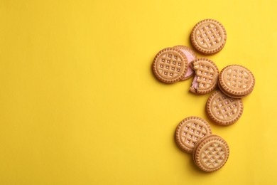 Photo of Tasty sandwich cookies with cream on yellow background, flat lay. Space for text