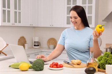 Photo of Beautiful overweight woman following online recipe to prepare healthy meal in kitchen