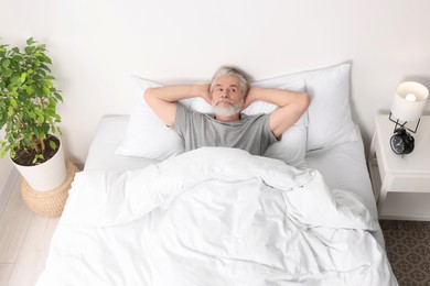 Photo of Man covering ears in bed and alarm clock on bedside table at home