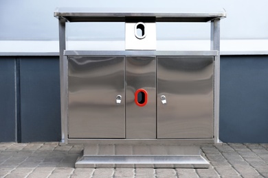 Photo of Modern metal recycling bin on street near building