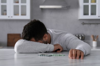 Photo of Man with antidepressant pills sleeping at white marble table in kitchen