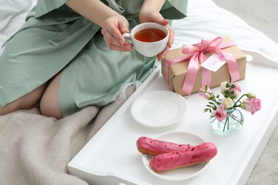 Photo of Tasty breakfast served in bed. Woman with tea, eclairs, gift box, flowers and I Love You card at home, closeup